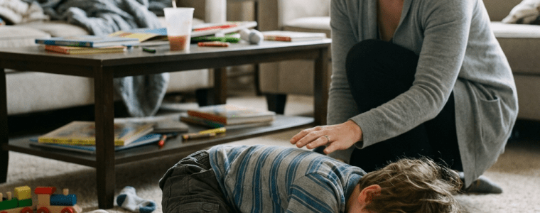Mother comforting upset young boy lying on the carpet in living room