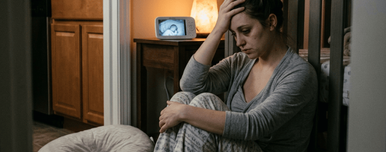 Pregnant woman sitting beside packed baby bag and crib monitor